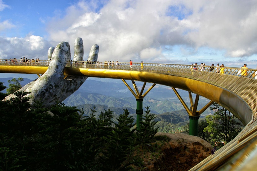 A single giant concrete hand can be seen holding the golden walkway of the bridge, as several people enjoy the view of jungle and hills that stretches for miles