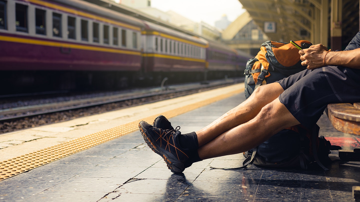 A backpacker waiting for a train while looking at a smartphone