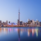 Toronto city skyline at twilight, with rainbow-colored reflections in the water and the CN Tower in the middle