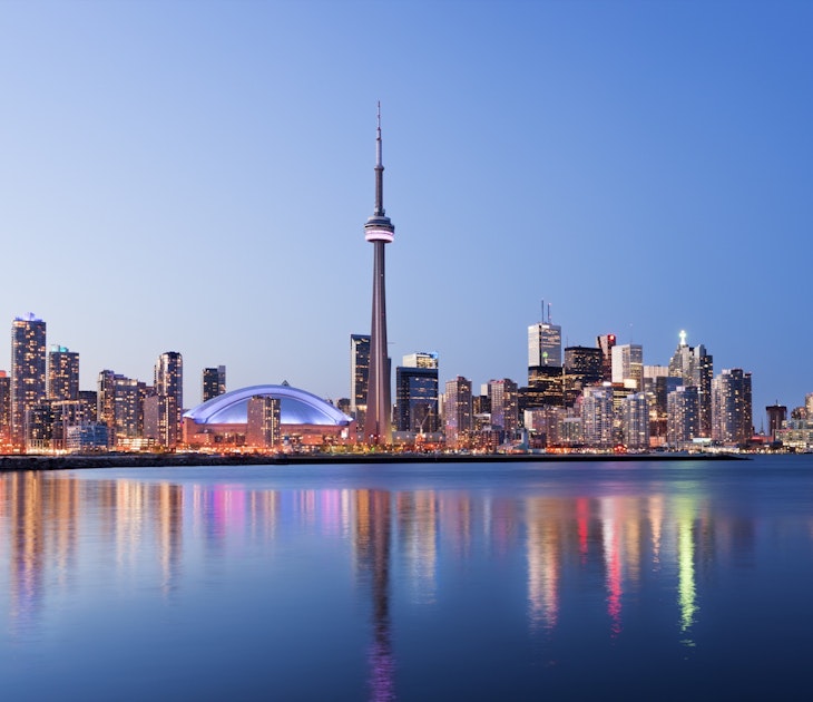 Toronto city skyline at twilight, with rainbow-colored reflections in the water and the CN Tower in the middle