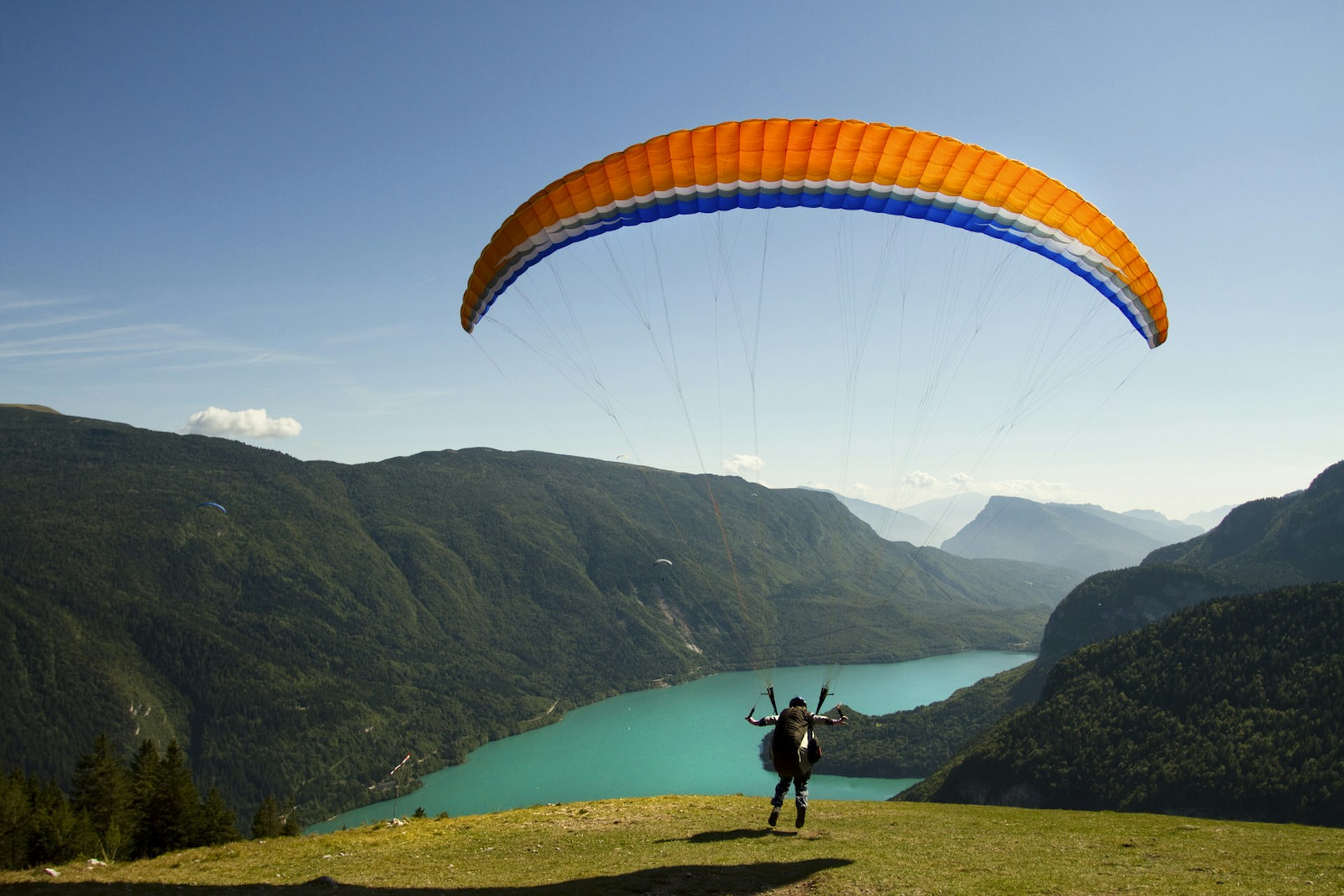 A paraglider takes off over the turquoise waters of Lake Molveno
