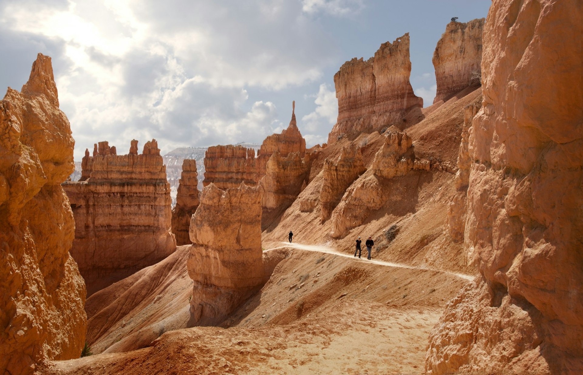 A few people walk in opposite directions through monumental rock formations in the red desert in Bryce Canyon, Utah. 