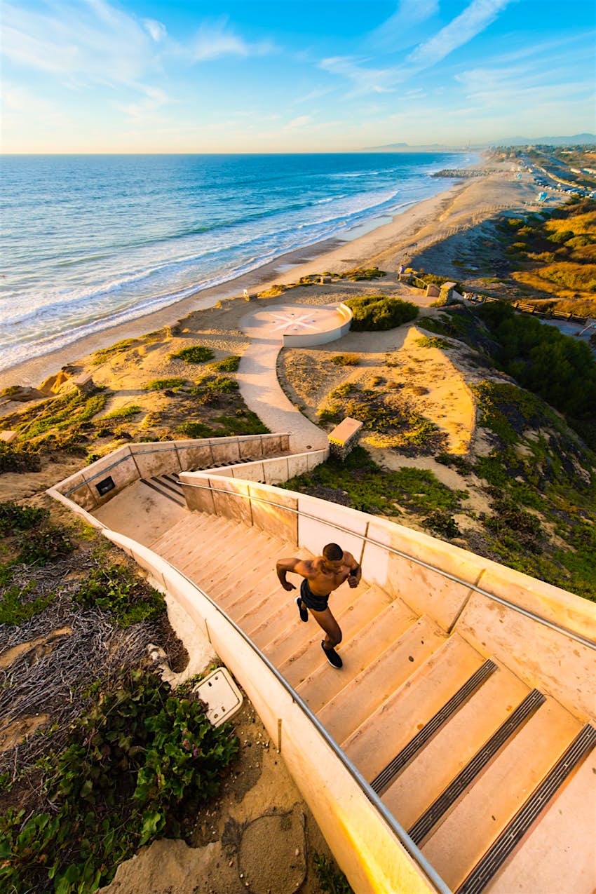 a man runs up a flight of stairs from the beach in the sun on a perfect weekend in San Diego