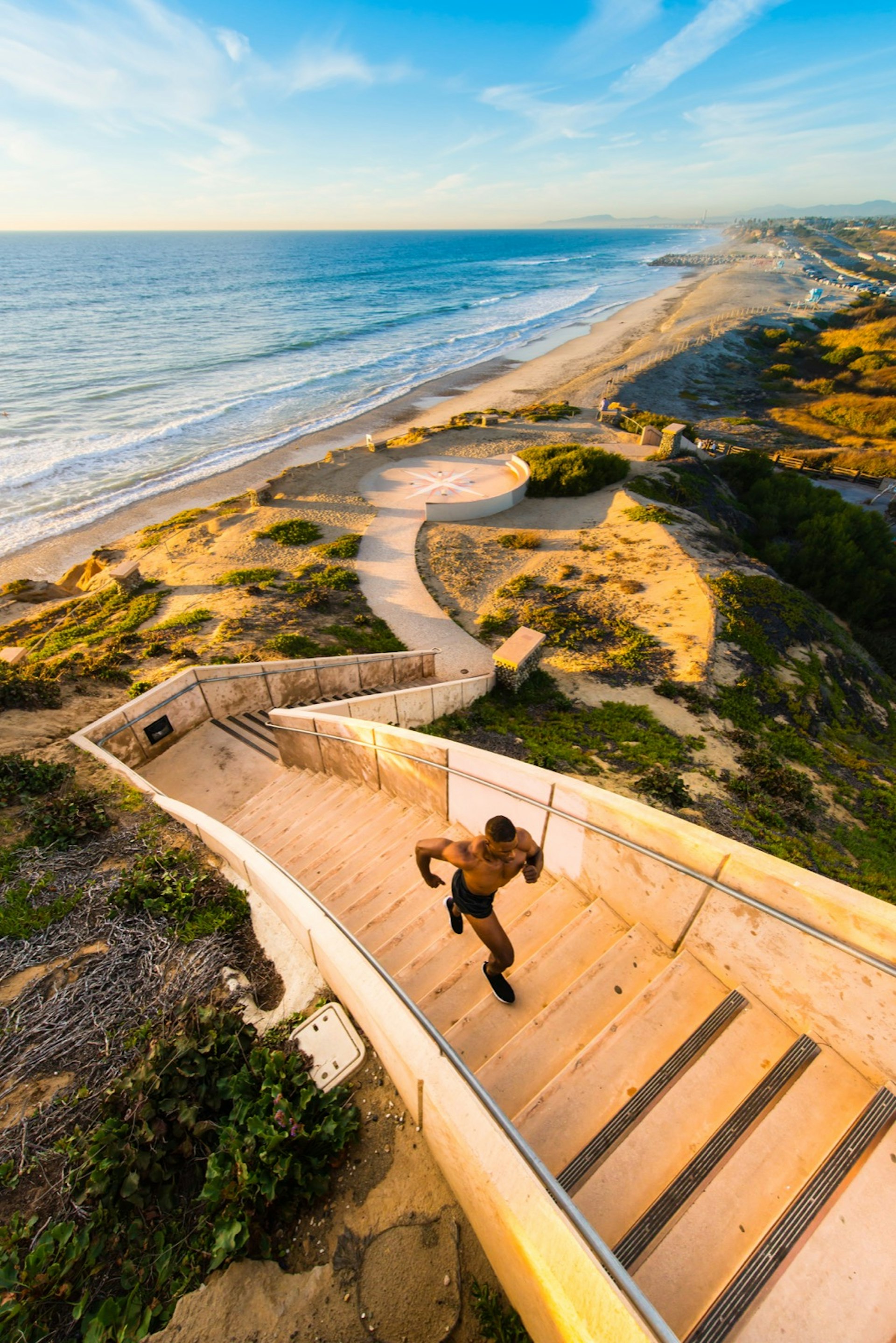 a man runs up a flight of stairs from the beach in the sun on a perfect weekend in San Diego