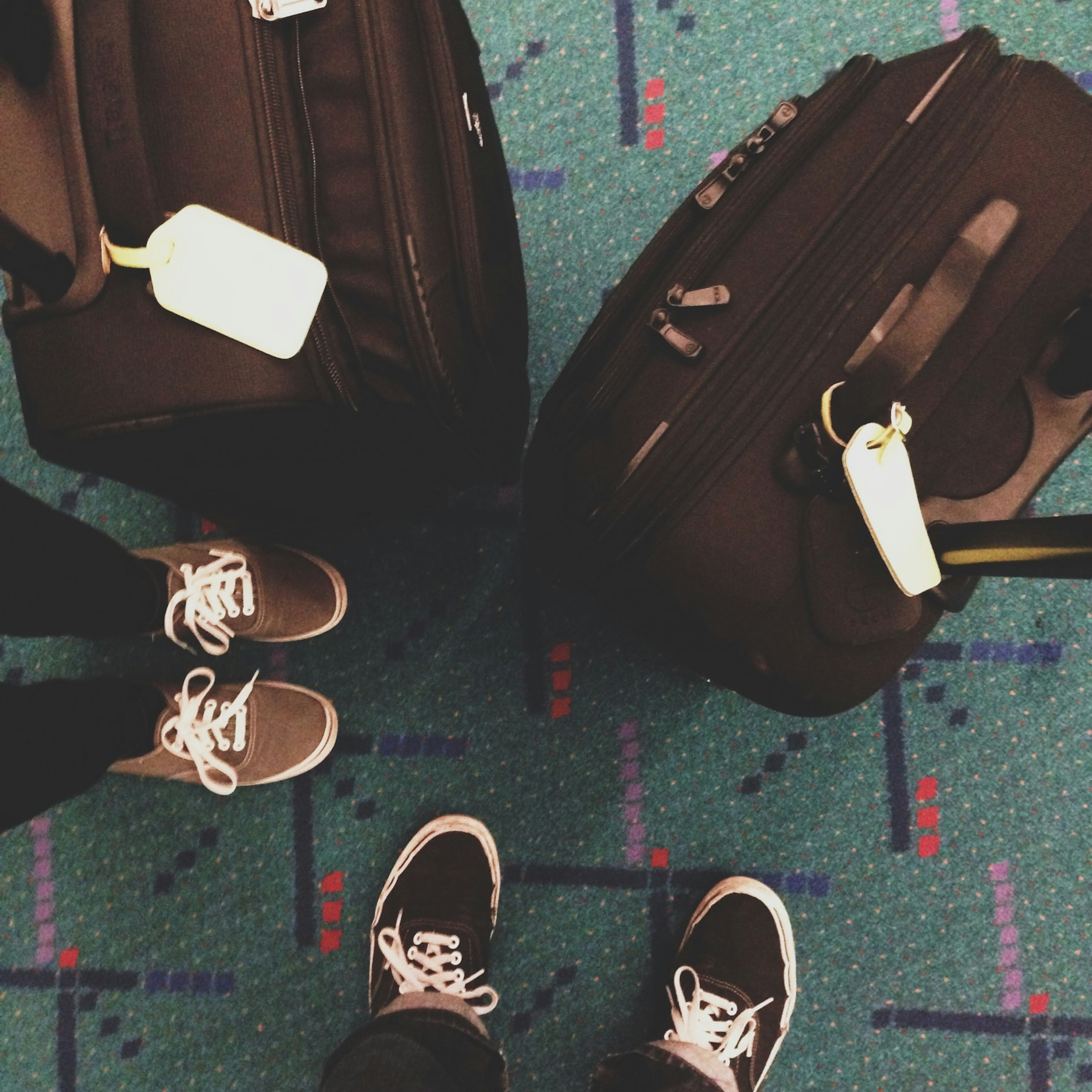 Feet and bags stand on a green carpet with very strange markings at PDX