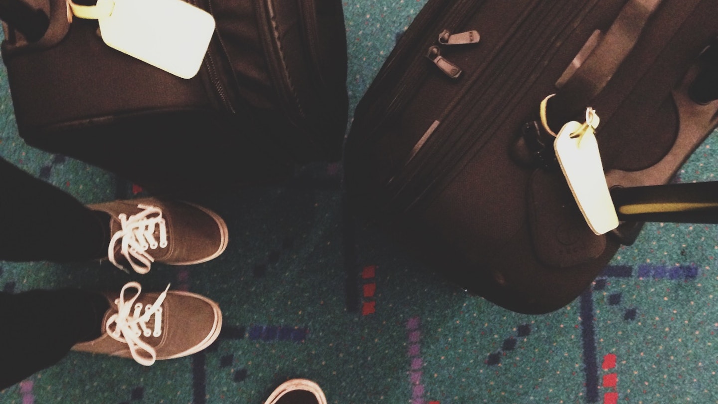 Feet and bags stand on a green carpet with very strange markings at PDX
