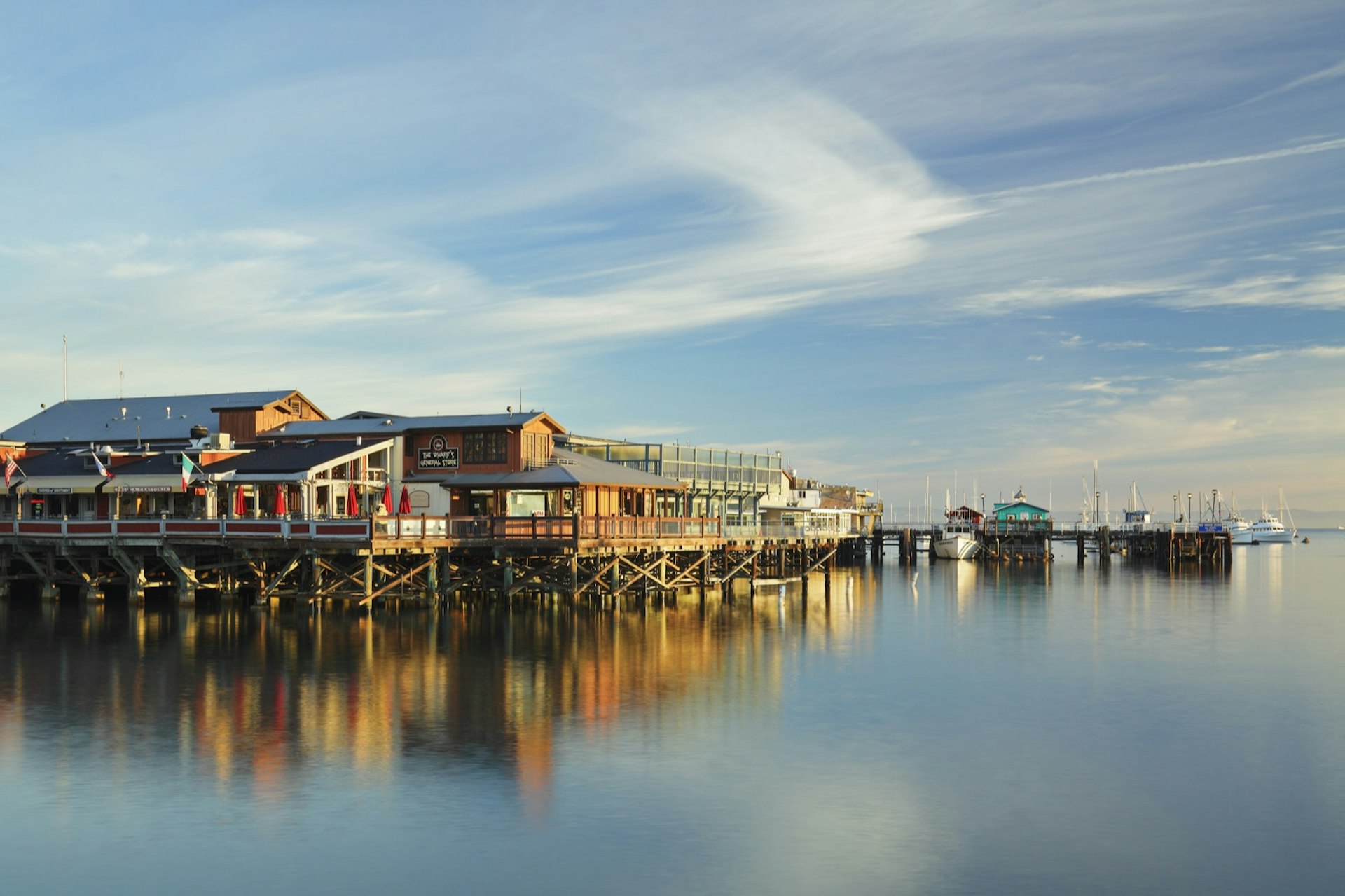 A view of wharf buildings on stilts with a reflection in the water that served as a Big Little Lies filming location in Monterey