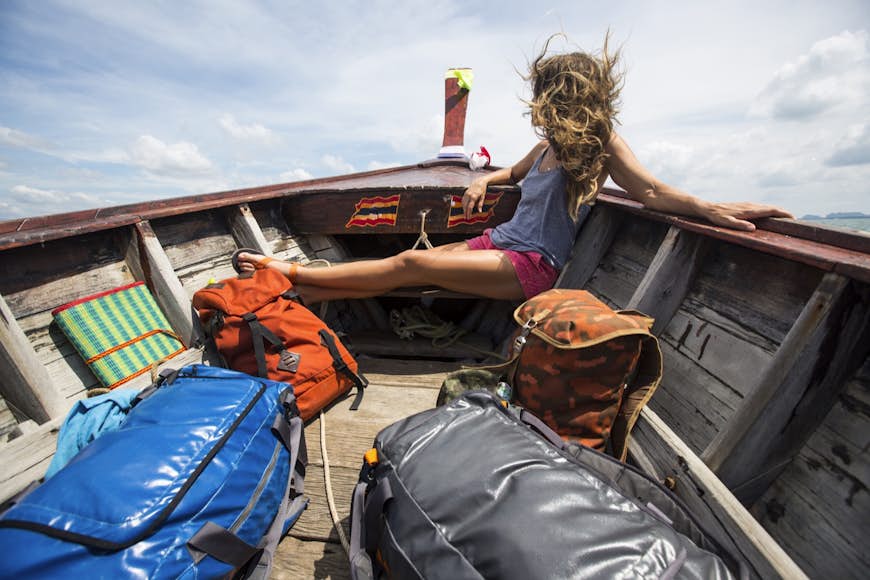 En kvinna sitter i fören på en båt med ryggsäckar;  hon tittar bort från kameran och håret blåser runt