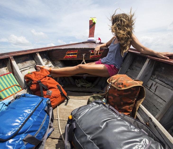 A woman sits in the bow of a boat with backpacks she is looking away from the camera and her hair is blowing around