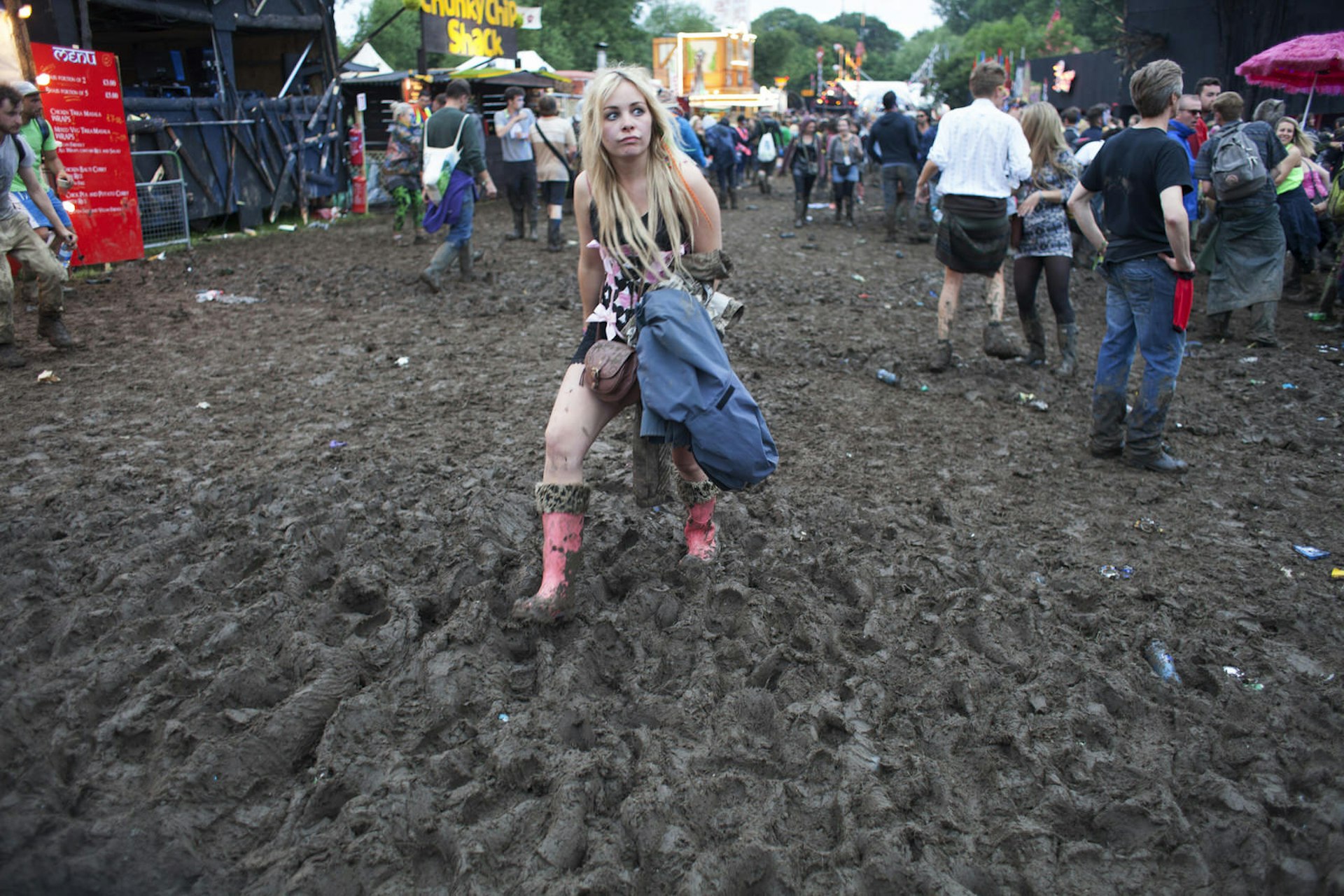 The scene in the Shangri-La section of the Glastonbury after a long night of dancing. Revellers make their way through the mud. A blonde woman sporting pink wellies with leopard trim is happily wading through
