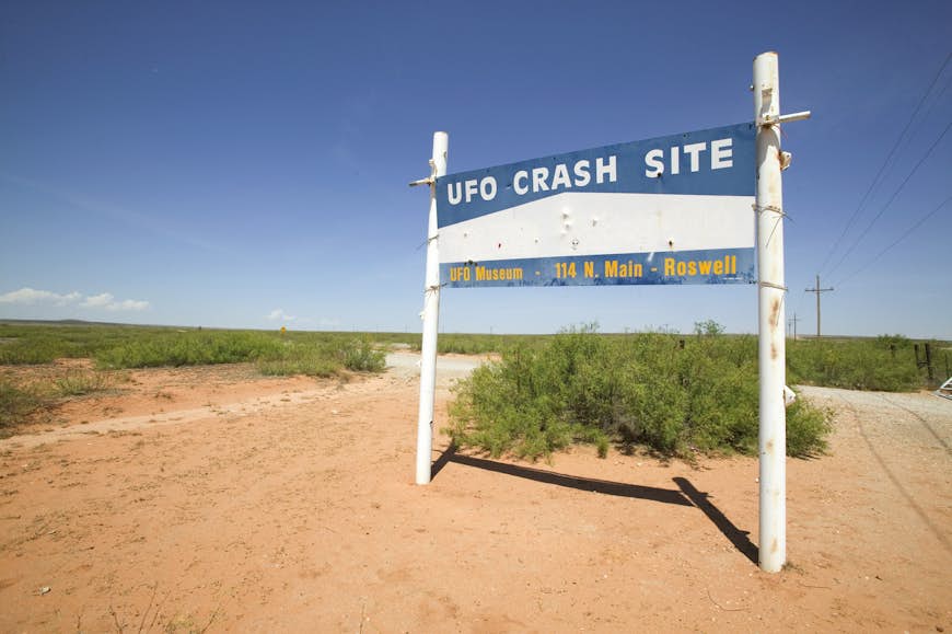 A sign that says 'UFO Crash Site' stands to the side of a dusty track
