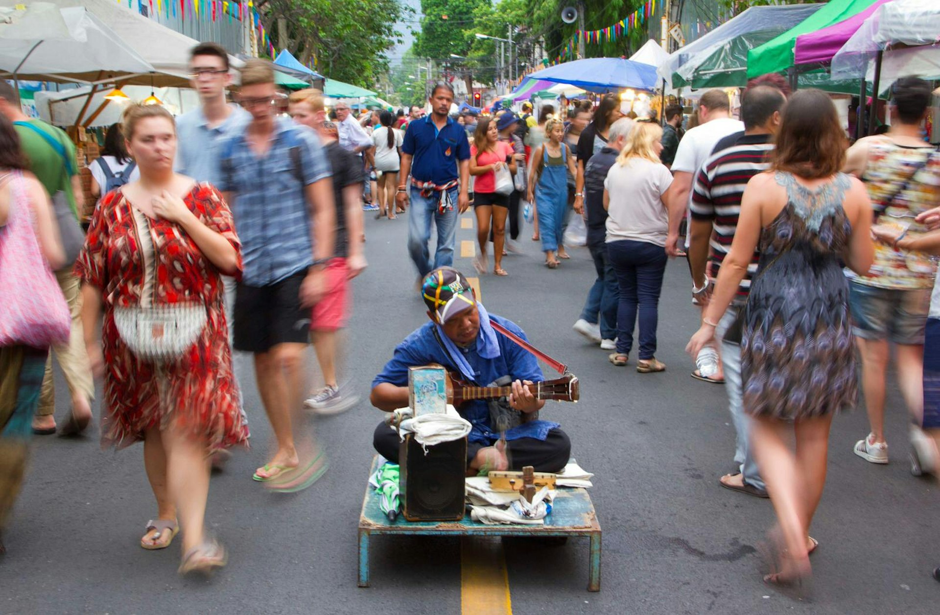 People walk past a man playing a guitar at the Sunday Night Market on Rachadamnoen Rd in Chiang Mai, Thailand.