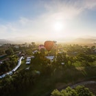 The sun rises over a verdant green valley while a red hot air balloon floats above in Temecula Valley