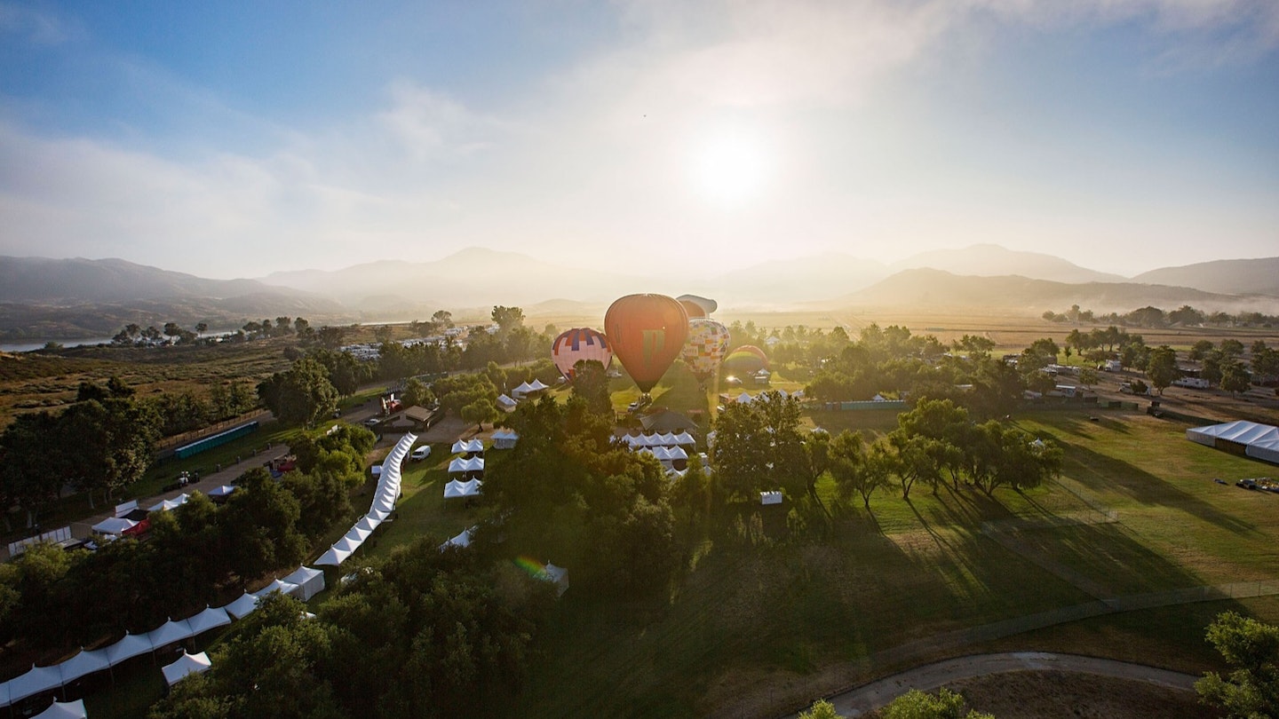The sun rises over a verdant green valley while a red hot air balloon floats above in Temecula Valley