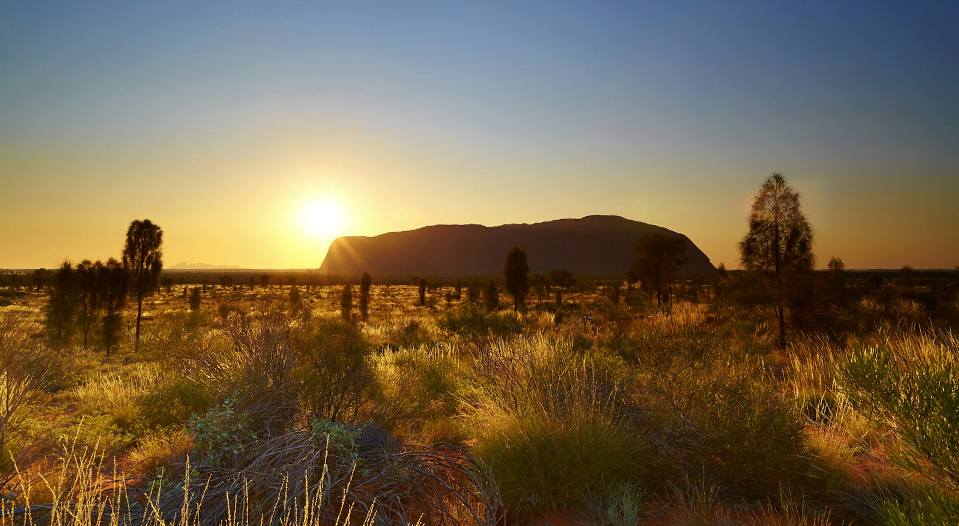 Sunrise at Uluru, in the heart of Australia's Outback. A plain of grass in the foreground stretches away towards the horizon and great limestone mass that is Uluru