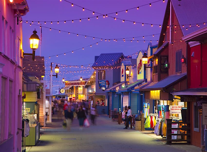 twinkle lights sparkle above a street lined with wooden structures and people walking in Monterey, California