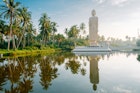 The Tusnami statue a tall white buddha on a white platform is perfectly reflected in the pool below and surrounded by palm trees in Sri Lanka
