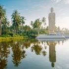 The Tusnami statue a tall white buddha on a white platform is perfectly reflected in the pool below and surrounded by palm trees in Sri Lanka