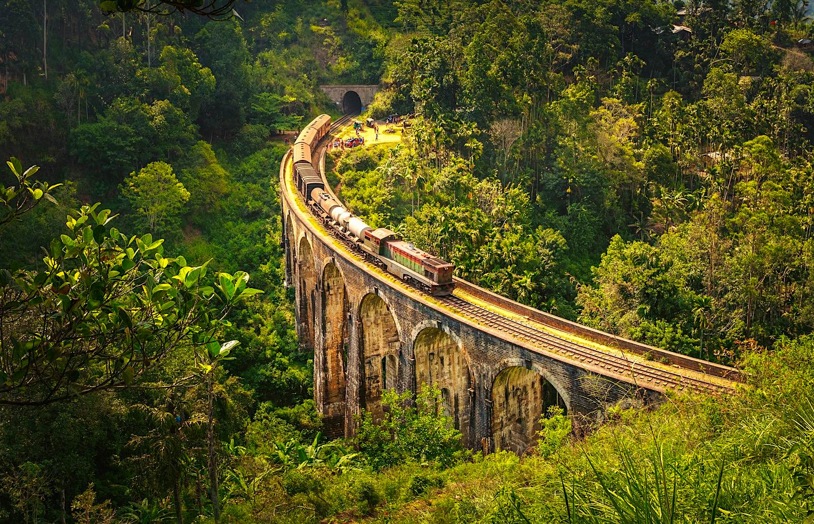 An arched bridge on which a train rumbles cutting through the rainforest in Sri Lanka