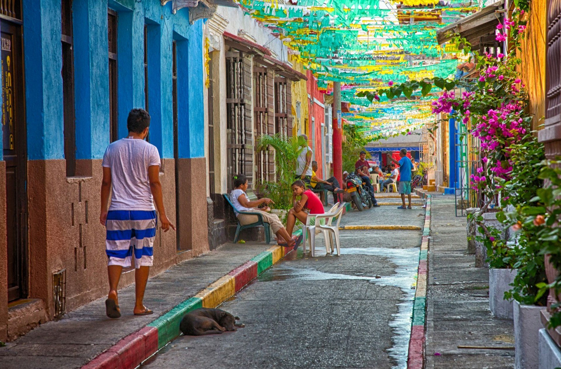 People on a small street lined with pink flowers and brightly painted buildings; free things to do in Cartagena