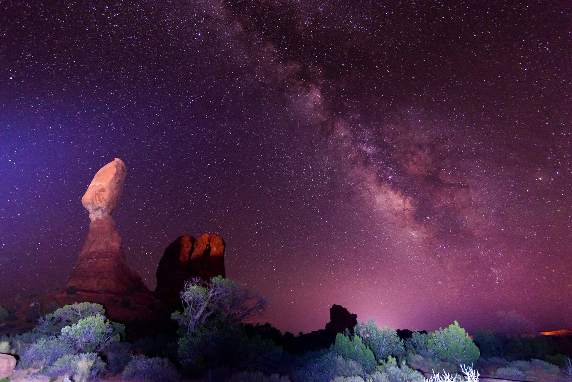 The Milky Way appears in the purple night sky above a rock formation in Utah