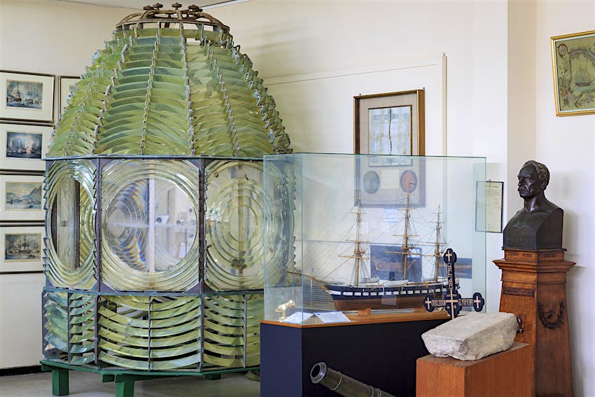 A lighthouse lens sits next to a small model boat at the Hellenic Maritime Museum in Piraeus, Greece.