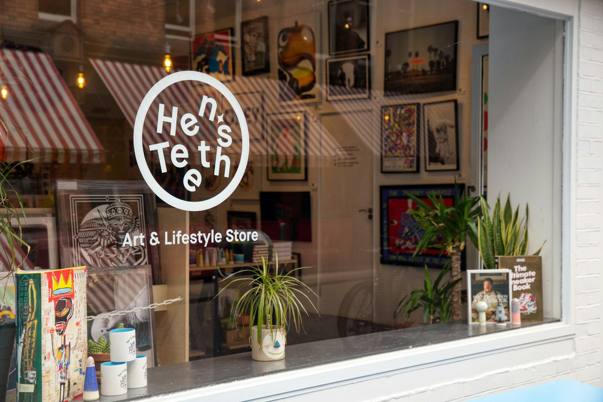 Dublin independent shops - Hen's Teeth shop front which is painted white with a large glass window featuring the Hen's Teeth logo. Behind the window we can see lots of framed artwork and some plants and candles