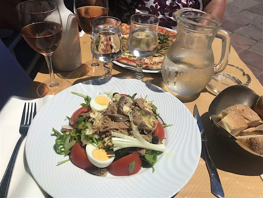 Spending diary Nice - Salad Niçoise and a pizza, two glasses of rose wine and a basket of bread on a table in the sun.