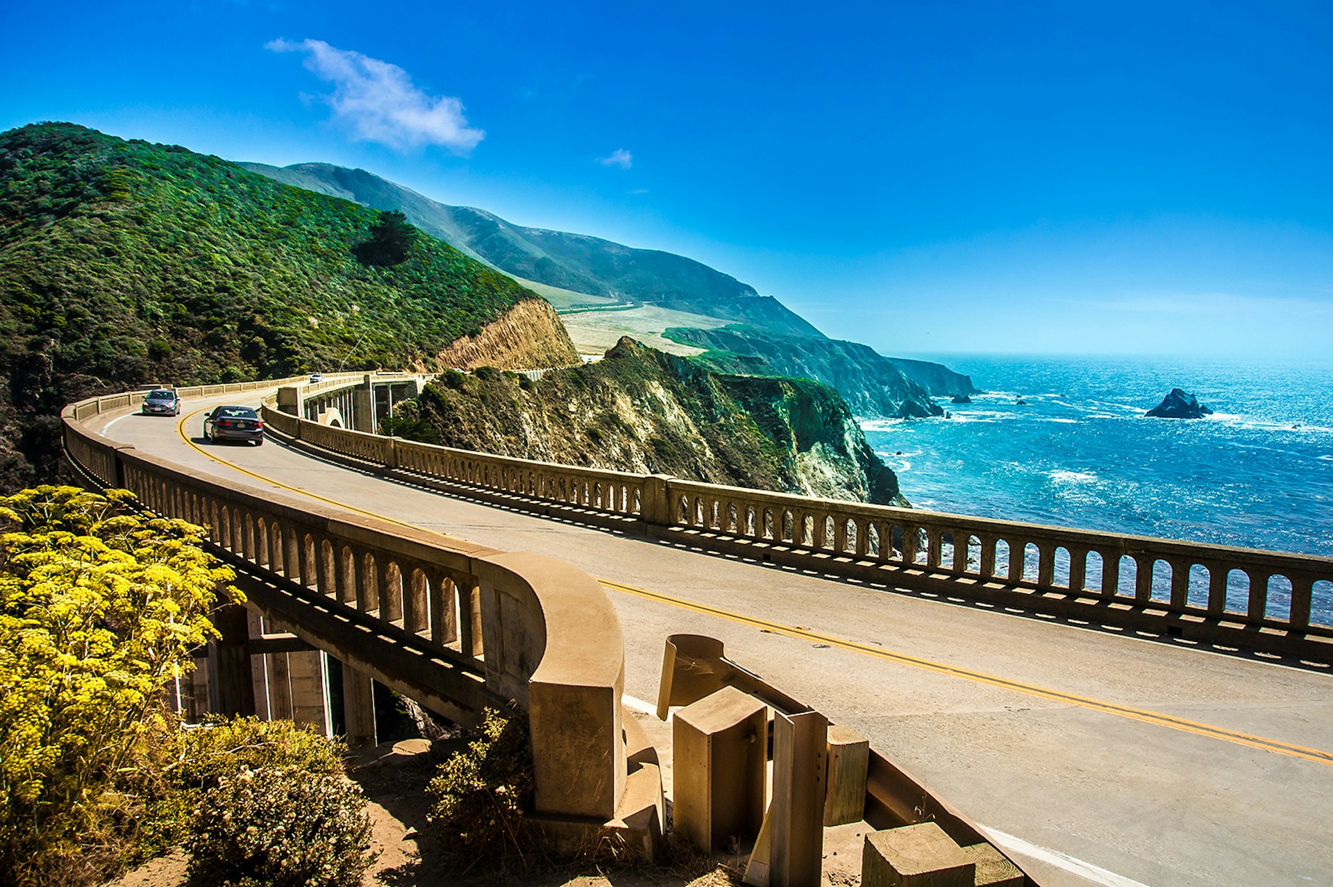 Western US road trip - A winding stretch of Highway 1 passes over a bridge with the Pacific Ocean to the right; it's a sunny day. California, USA.