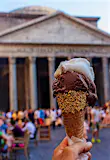 A hand holding a delicious cone of Italian gelato in front of the Pantheon in Rome