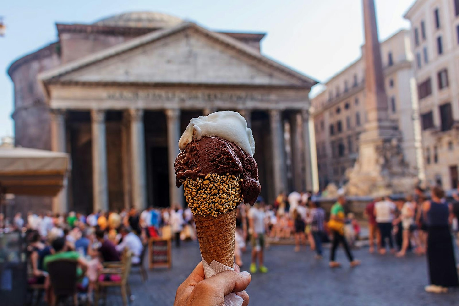 A hand holding a delicious cone of Italian gelato in front of the Pantheon in Rome