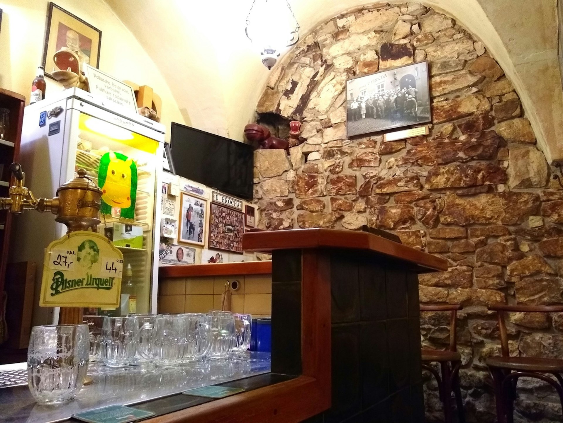 An arched stone wall marks an underground bar with an old brass tap and glass steins on the bar