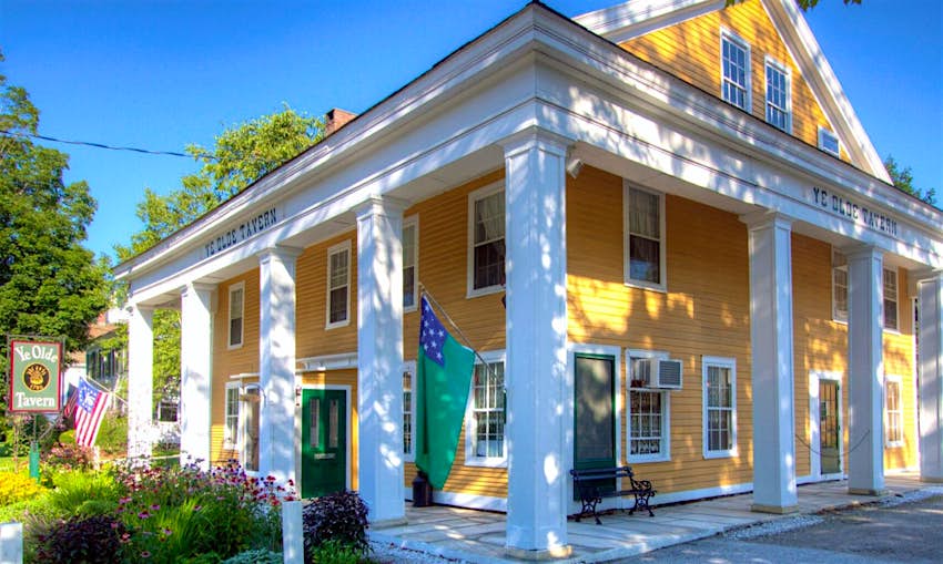 Features - Ye-Olde-Tavern-2c1f7c4705f3 A yellow house-like building with white eaves and columns against a blue sky