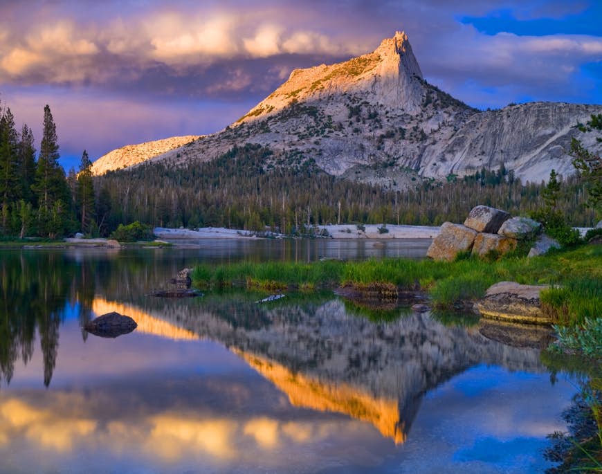 Snow-covered Cathedral Peak is reflected in a lake at Yosemite National Park at sunset