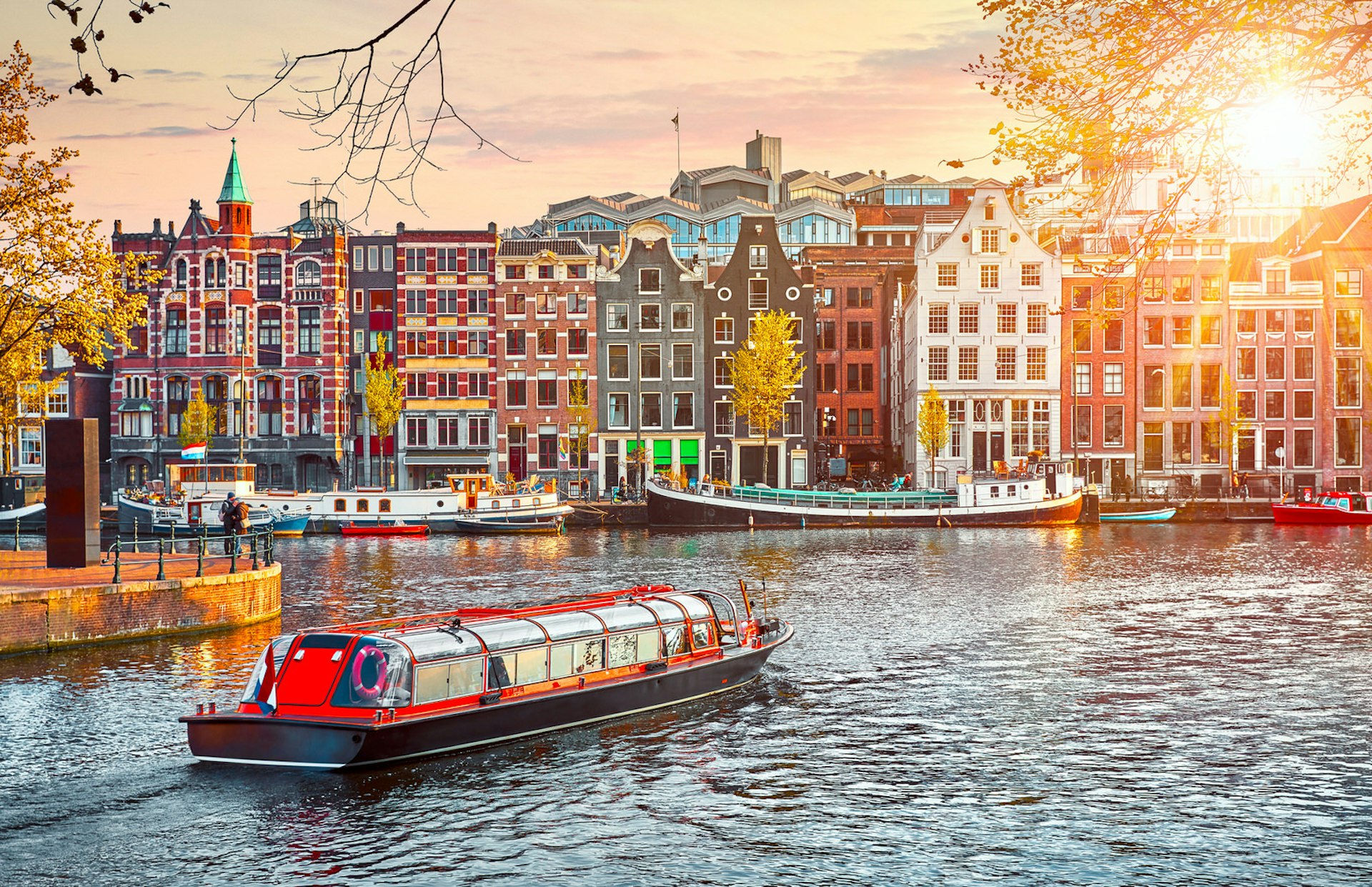 A pleasure boat navigating a waterway in Amsterdam, a key Killing Eve season two location; the canal is lined with colourful medieval houses and boats.