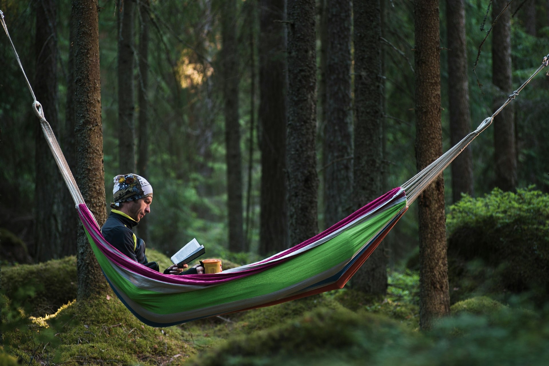 A man reads in a hammock in the woods while camping. 