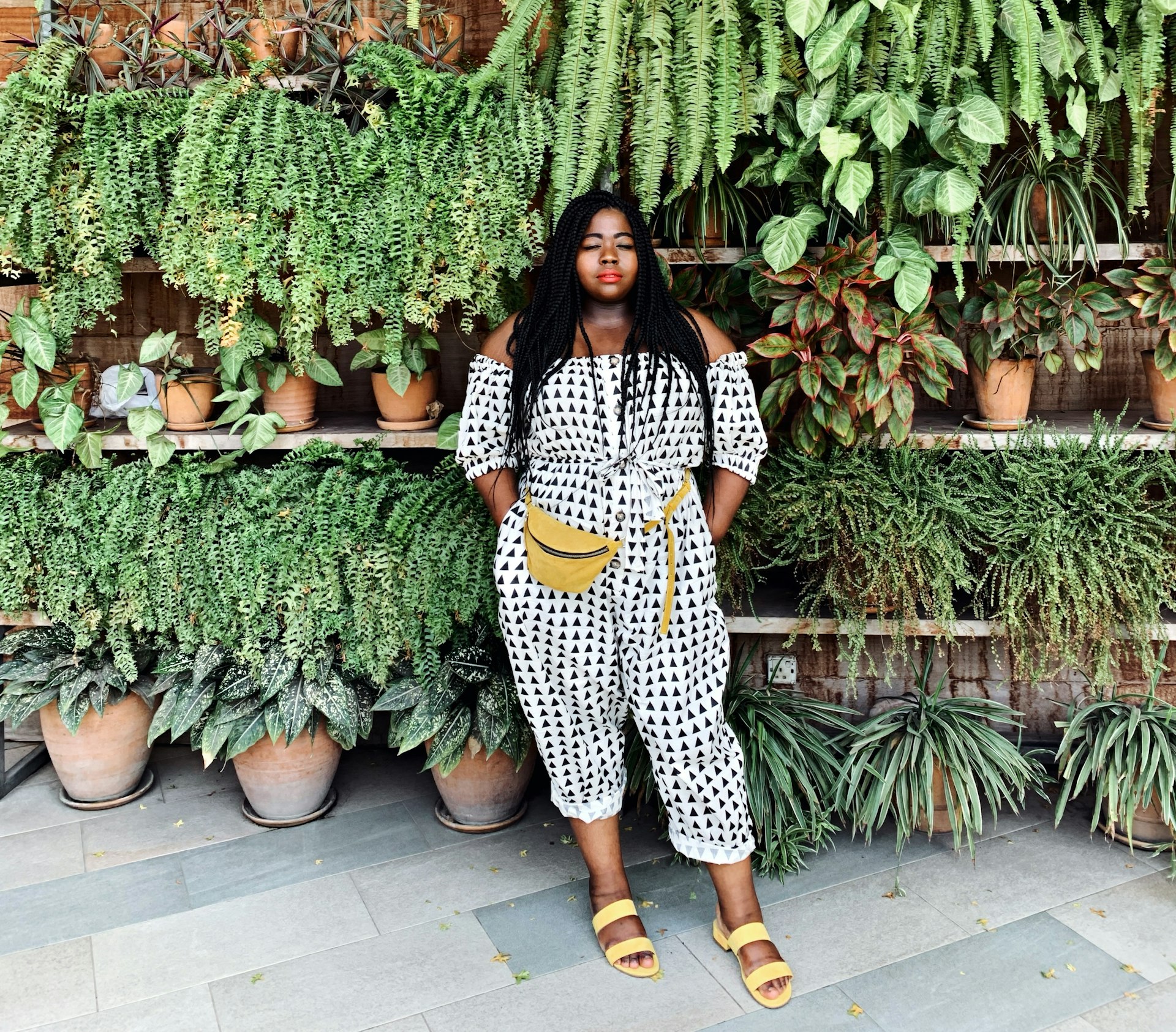 Stephanie Yeboah posing in front of plants in a black-and-white jumpsuit with a yellow bumbag and matching sandals