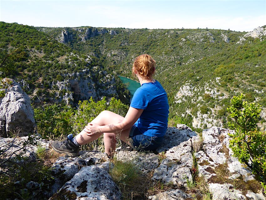 The writer, a woman with red hair wearing shorts and t shirt, looks down on the green river of the gorge, surrounded by high cliffs.