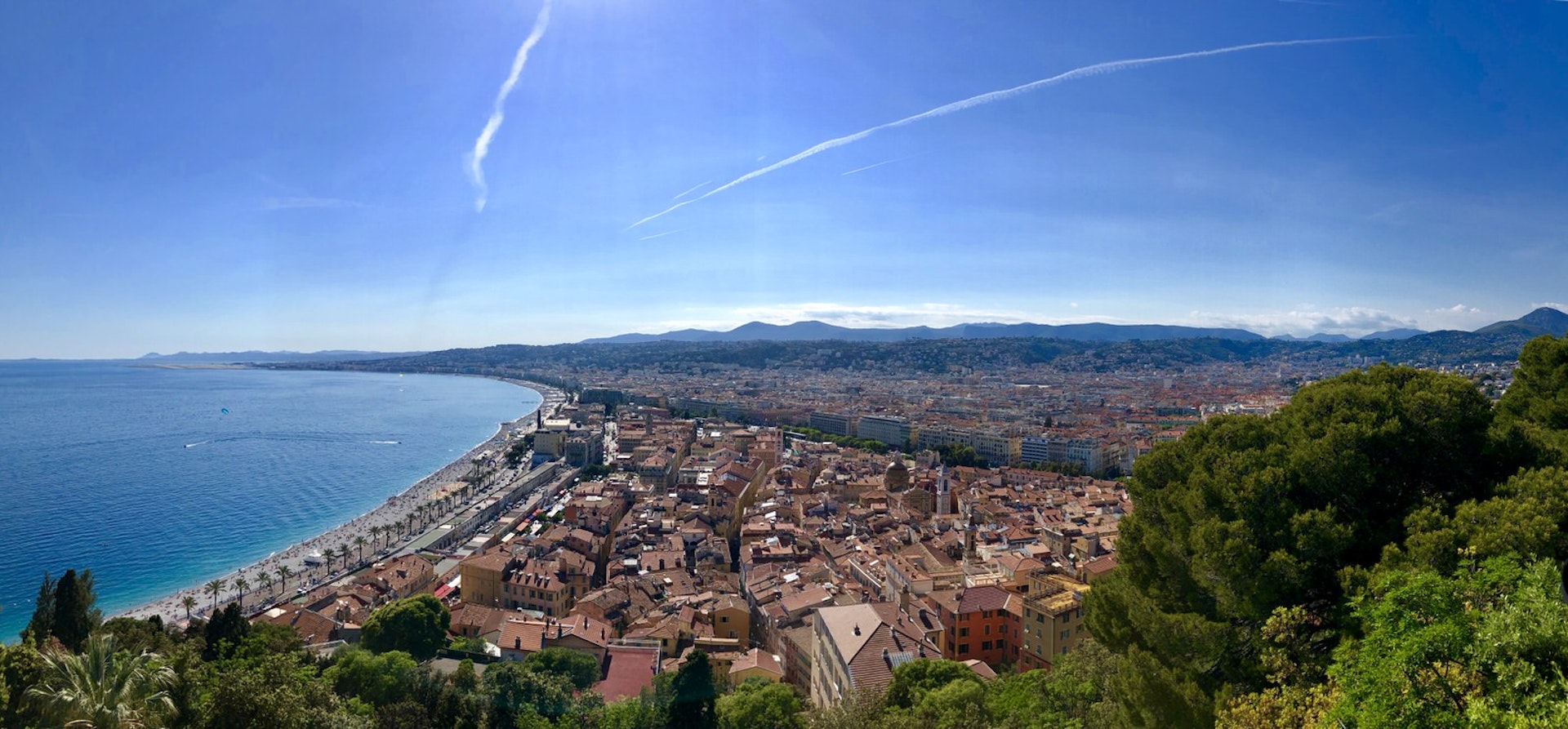 Spending diary Nice - A panorama shot of Nice on a sunny day from up high. On the right, there are red rooftops, on the left the promenada, beach and sea.
