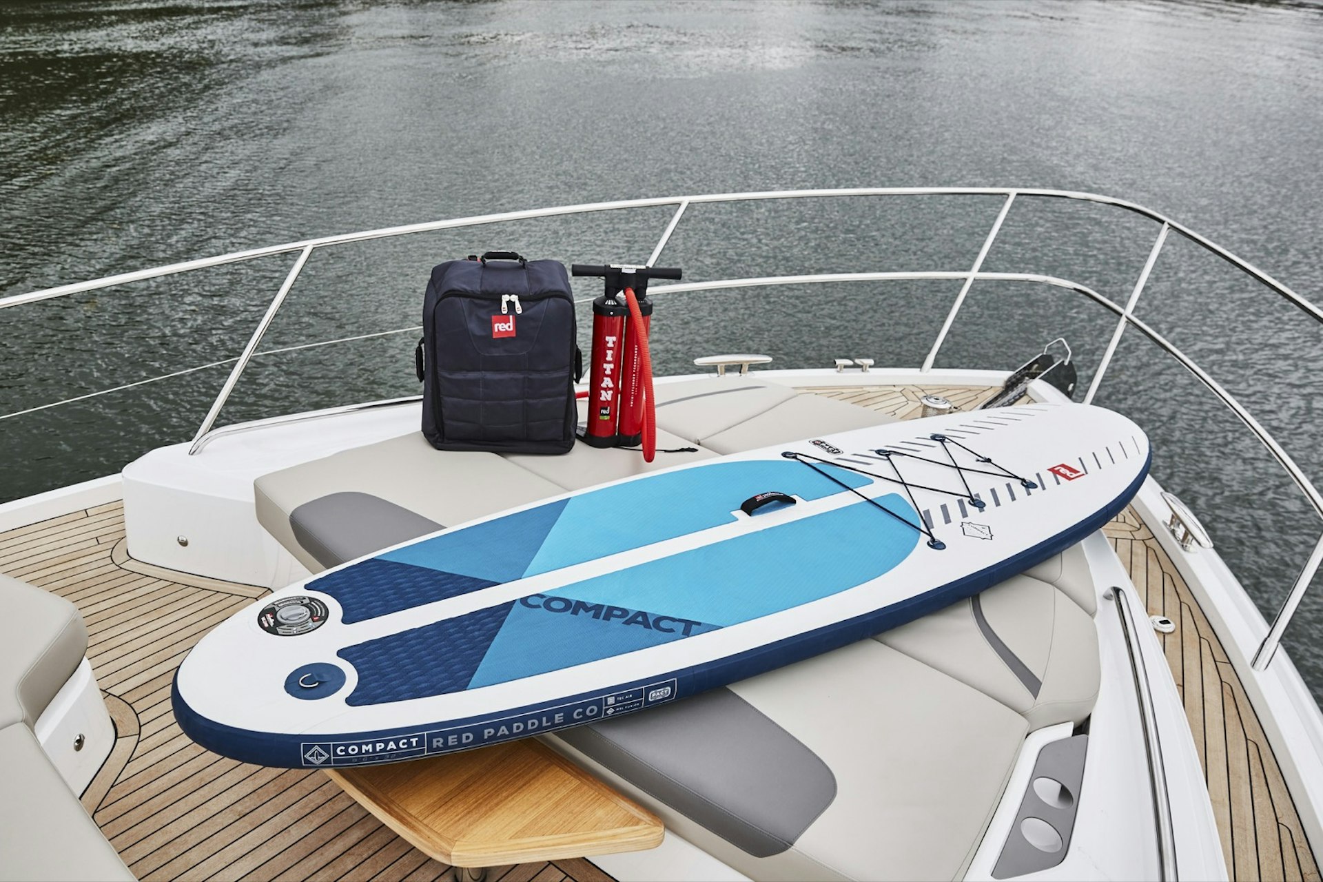 a paddleboard, pack and air pump rest on the bow of a boat