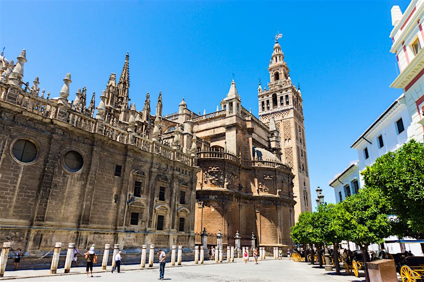 The huge Gothic exterior of Seville's Cathedral; at one end is its Giralda bell tower, resembling a minaret with a delicate brick-pattern decoration.