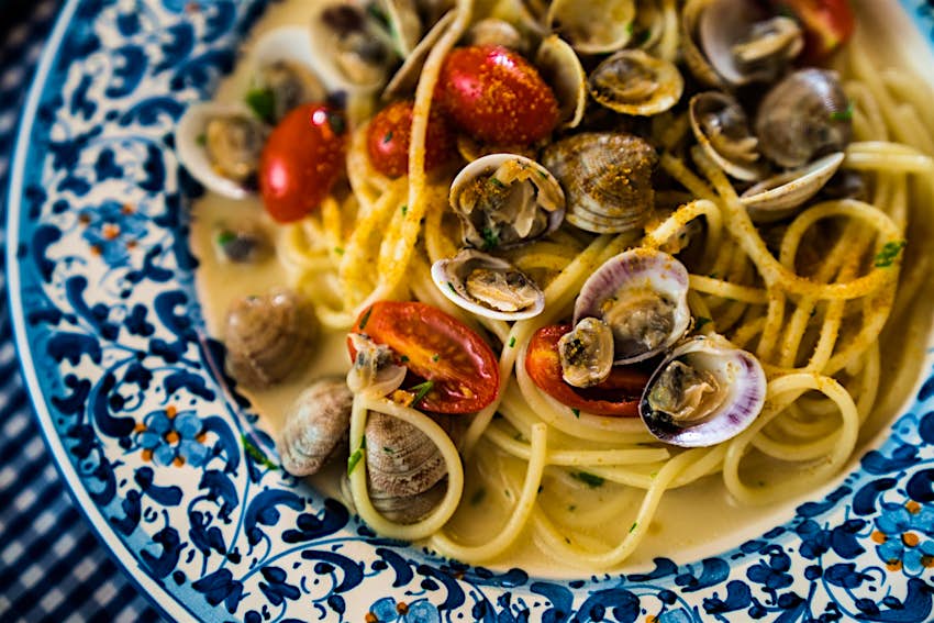 A blue-and-white plate filled with spaghetti noodles, clams and red tomoatoes; best things to do in Sardinia