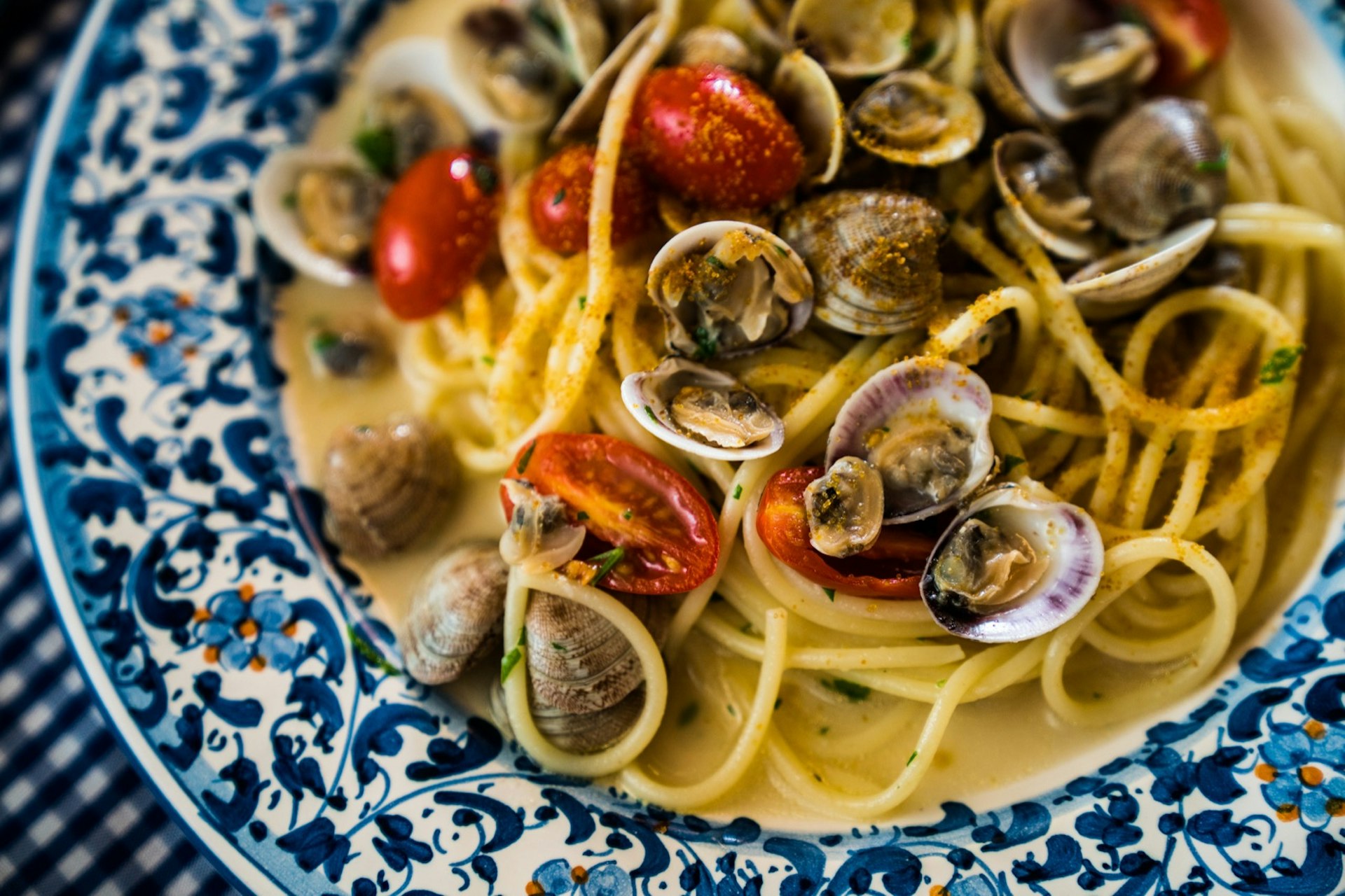 A blue-and-white plate filled with spaghetti noodles, clams and red tomoatoes; best things to do in Sardinia