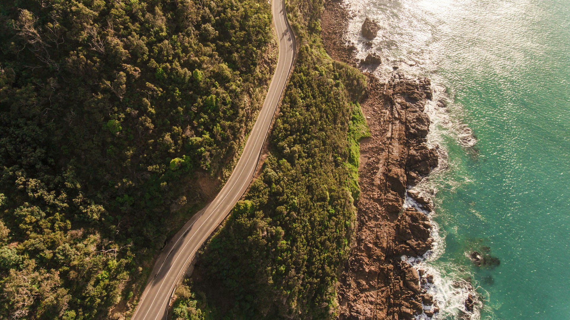 An aerial view of the Great Ocean Road, with a strip of tarmac running alongside the turquoise sea