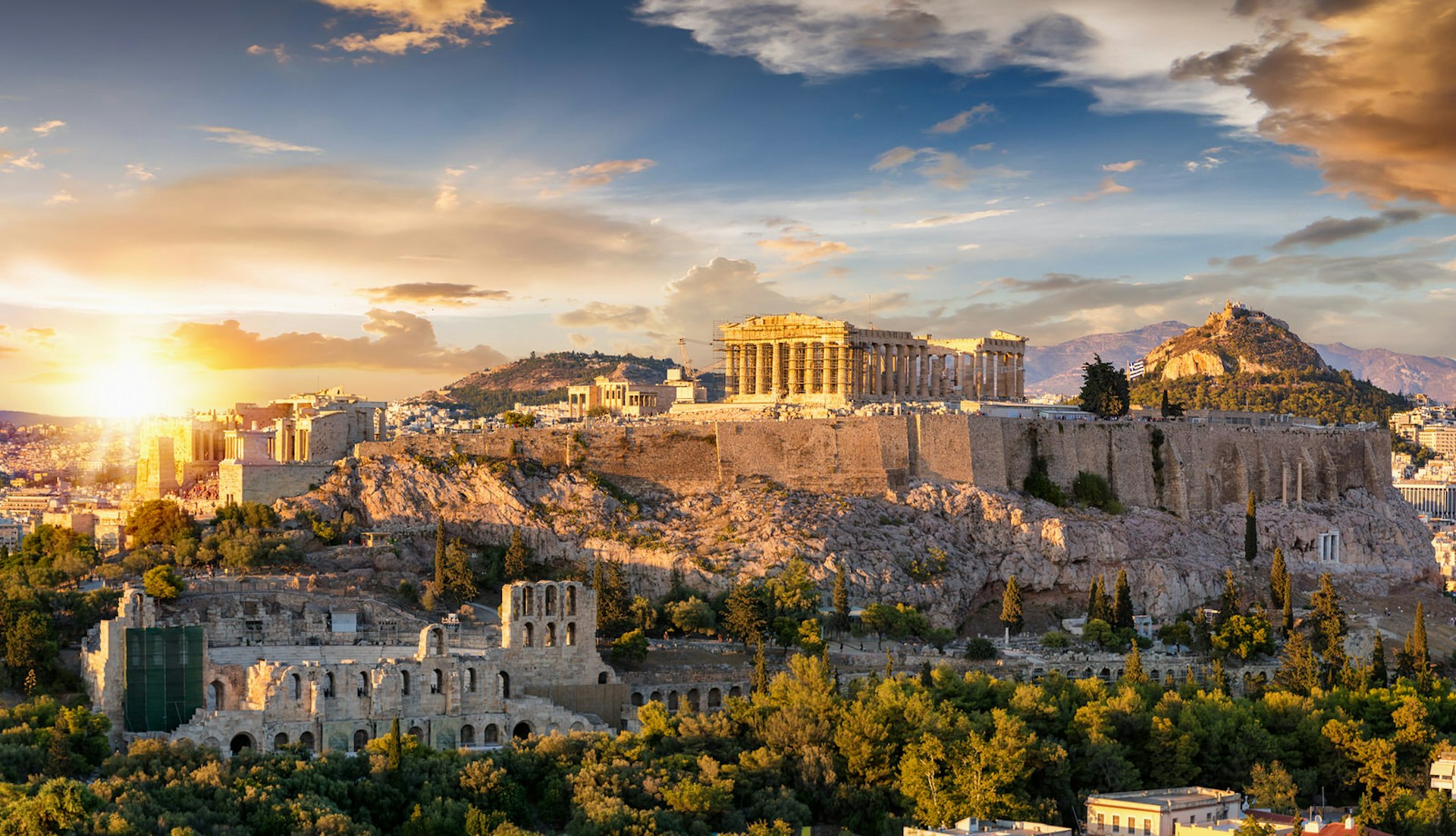 The Acropolis of Athens, Greece, crowned by the columns of the Parthenon temple, on top of a hill during a summer sunset.