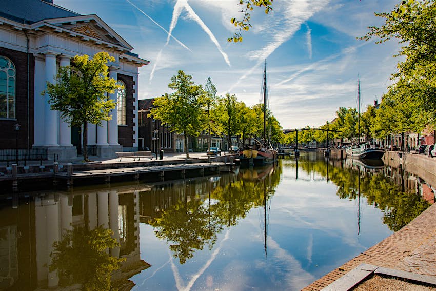 A canal in Schiedam with a bridge, trees and a white, grand-looking building visible