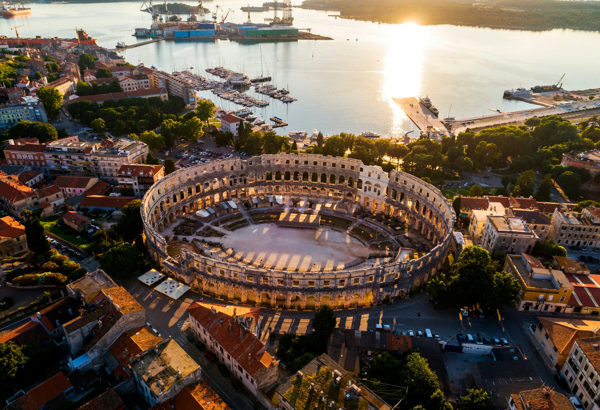 Pula Arena, Croatia, at sunset. The ruins of the Roman amphitheater are very well preserved. The circular structure is surrounded by houses with a glistening body of water beyond