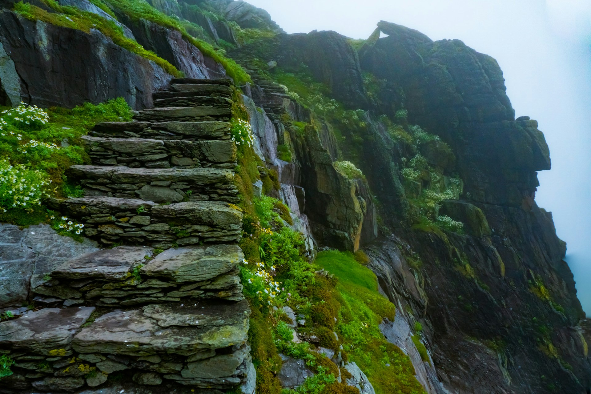 Stone stairs cut into the side of the mountain, covered in a moss on a misty day