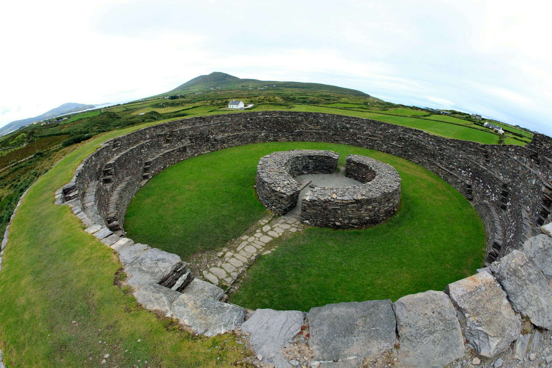 An ancient stone circle on grassy landscape surrounds a smaller stone circular fort.