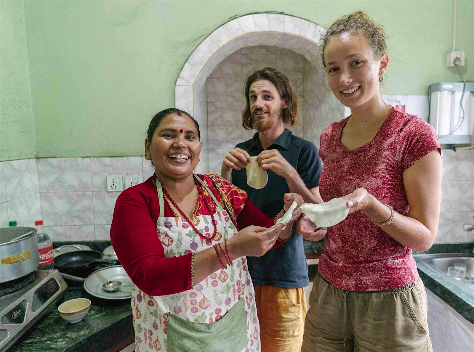 Ein männlicher und ein weiblicher Reisender halten Chapatis, während sie mit einer Frau posieren, die einen Kochkurs leitet